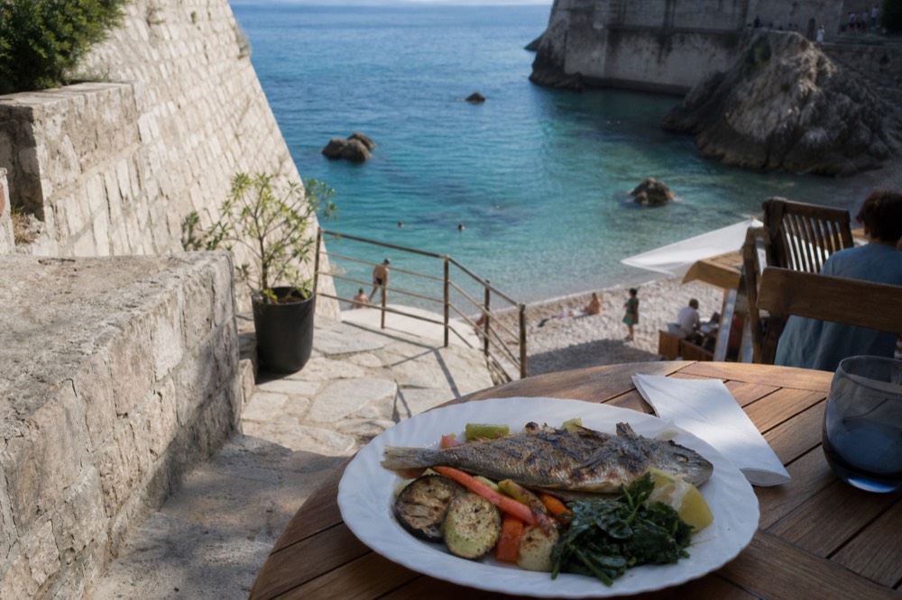 A plate of grilled fish and vegetables on a simple wooden table at a small restaurant