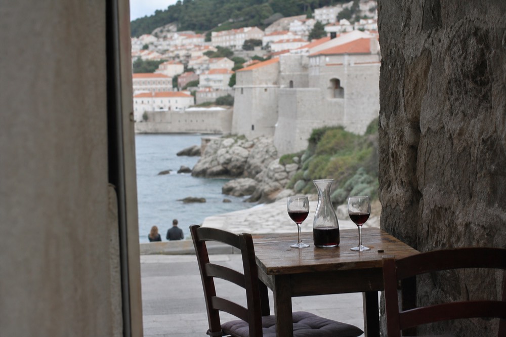 A carafe of red wine and two glasses on a rustic table beside a stone wall