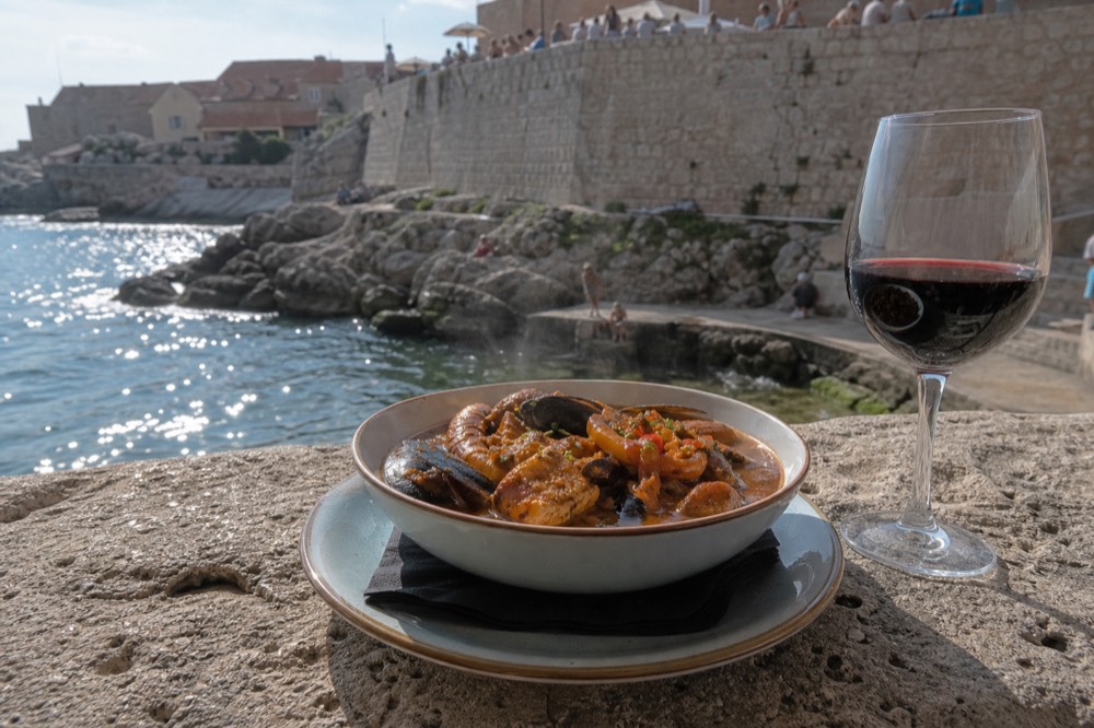 A bowl of steaming stew and a glass of red wine on a rustic restaurant table