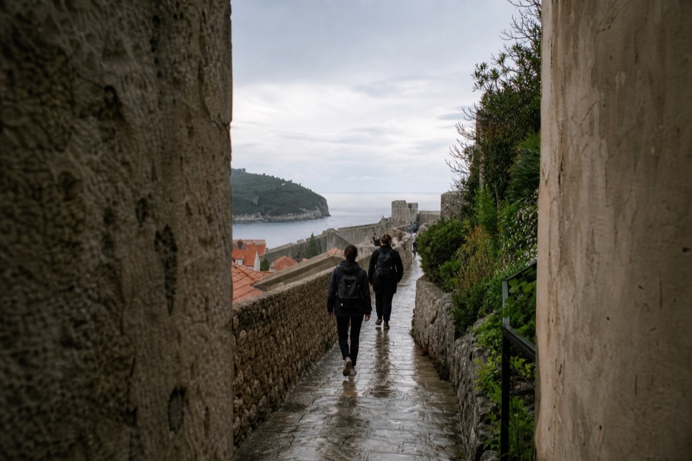 Walkers on the city walls path above red rooftops and the sea