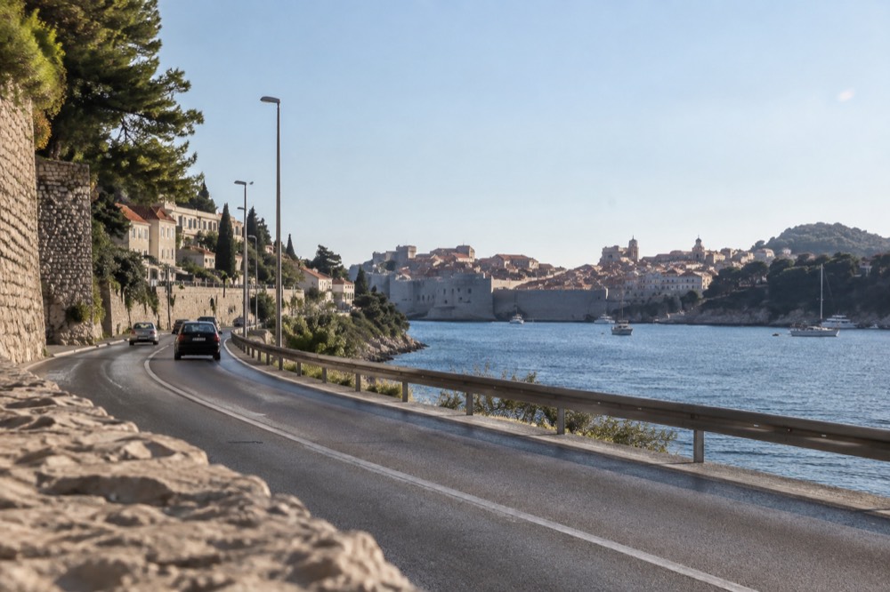 Coastal road curving around Gruž bay with the Old Town walls visible in the distance
