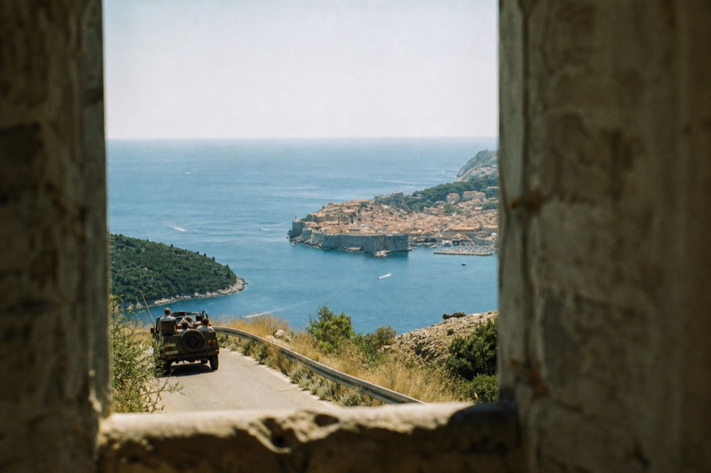 Open-air vehicle on a hillside road above Dubrovnik with the walled city below