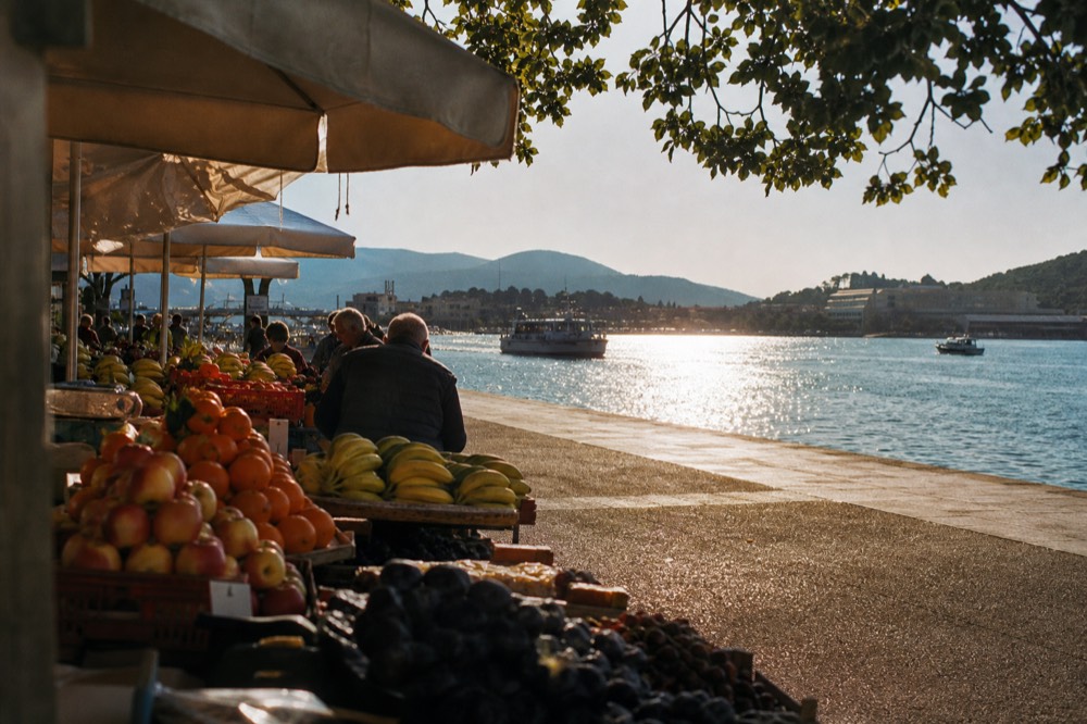 Market stalls with fruit and shade awnings beside the Gruž waterfront