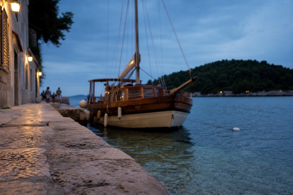 A wooden sailing boat moored in clear shallow water beside a green island