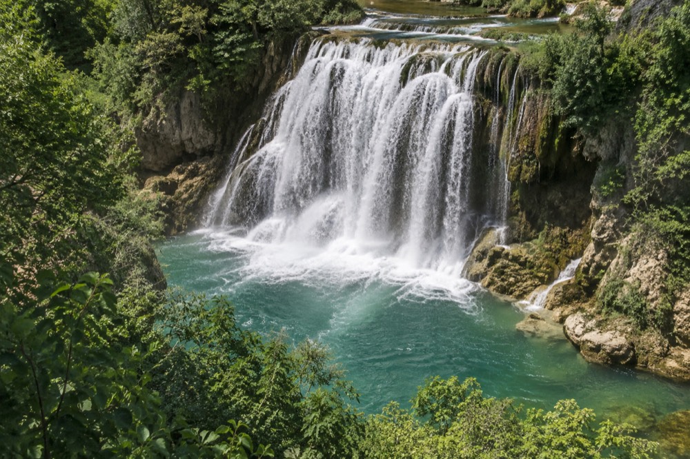 A wide waterfall pouring into a turquoise pool surrounded by green cliffs