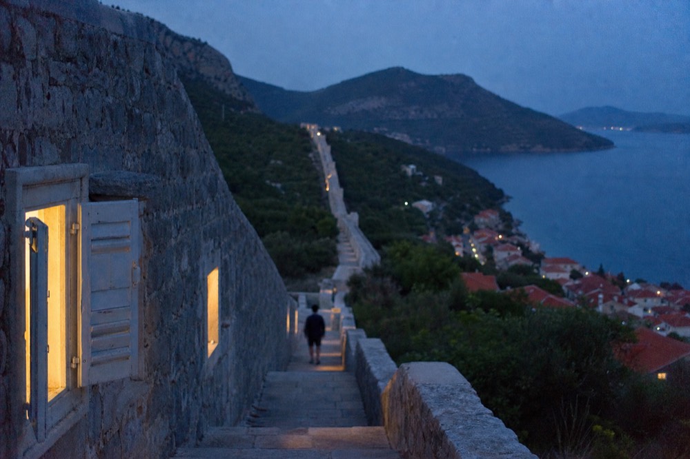 A long stone wall crossing a green hillside above a small coastal town