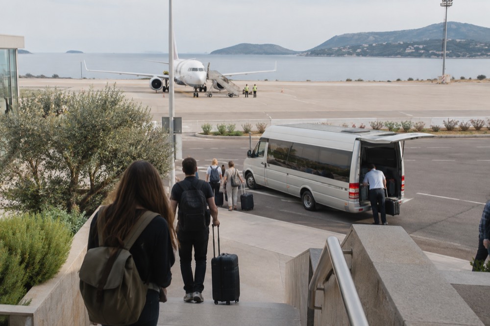 A shuttle minibus parked at an airport kerb with luggage being loaded