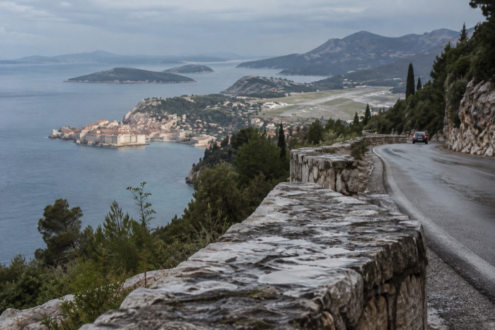 A coastal road winding above the Adriatic with a walled city in the distance