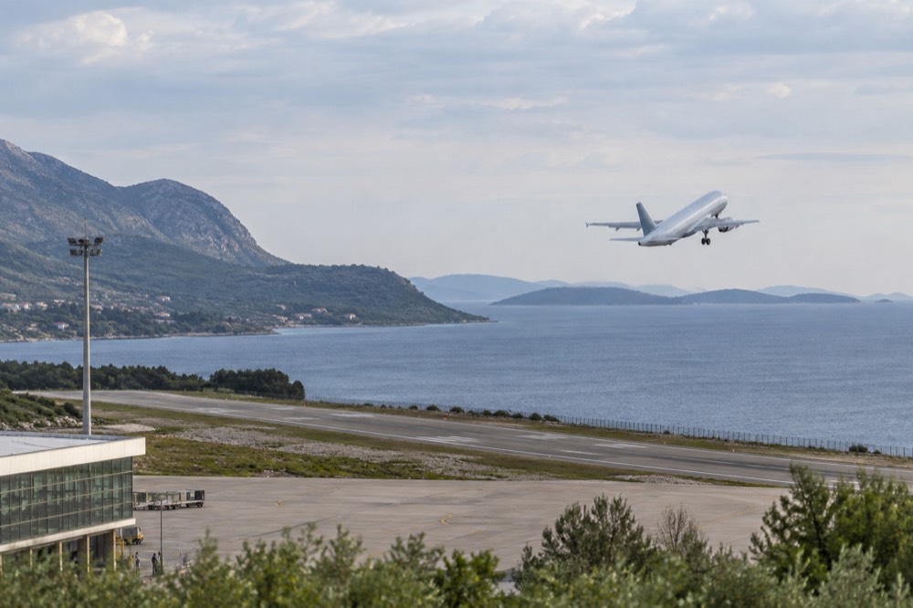 A narrow-body airliner climbing away from a runway above the sea