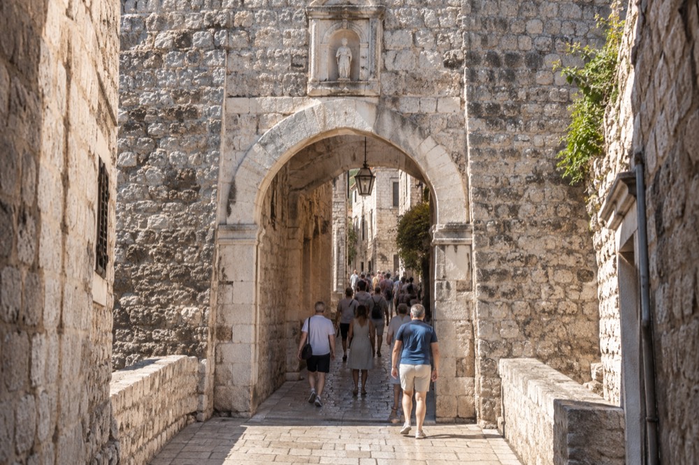A stone gate entrance to a walled old town with people walking through