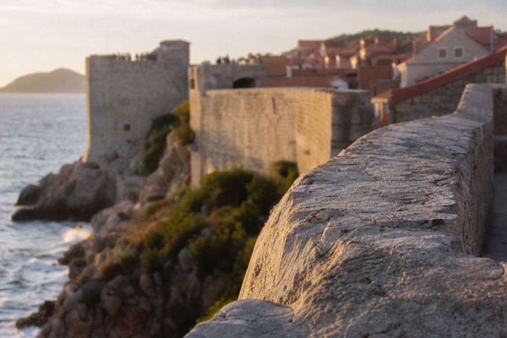 Stone city walls of Dubrovnik curving above the sea with red rooftops behind