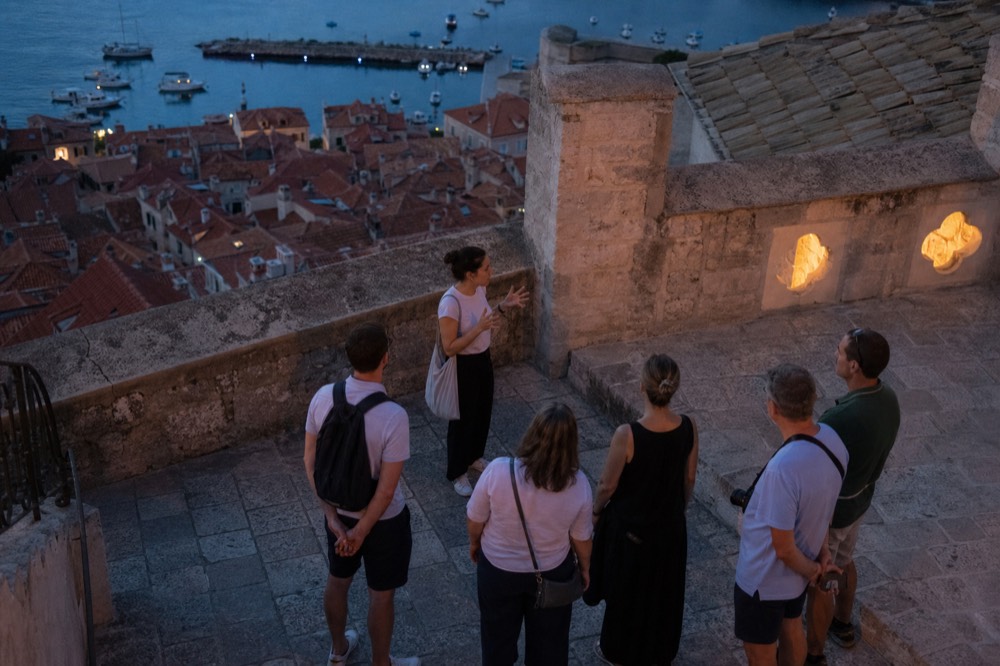 A guide speaking to a small group of visitors on a stone terrace above Dubrovnik