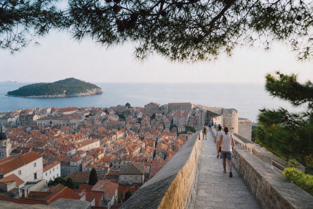 Walkers on the stone city walls path high above Dubrovnik's red rooftops