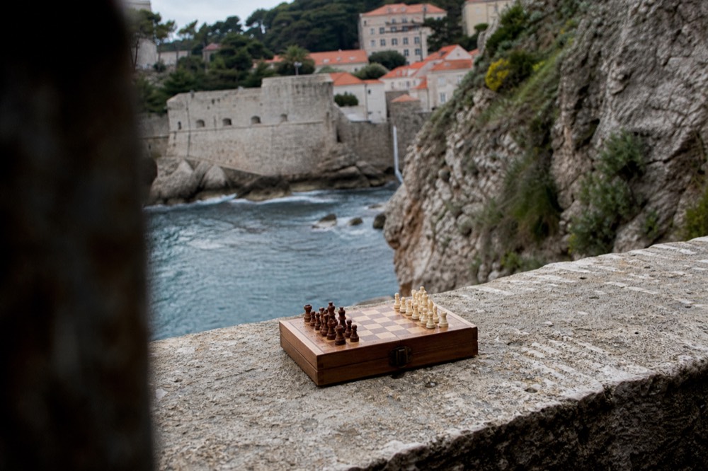 A folded wooden travel chess set resting on a stone ledge above the sea