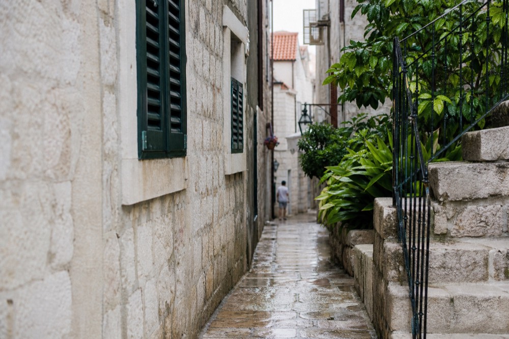 A quiet limestone lane inside Dubrovnik Old Town with shutters and stone staircases