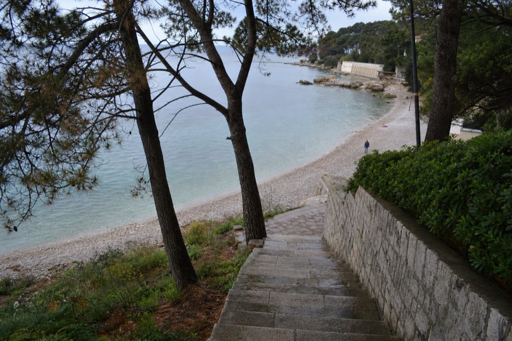 A pebble beach on Lapad bay with calm water and pine trees in spring