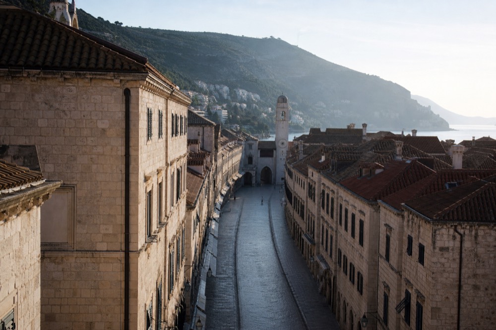 Empty Stradun street in Dubrovnik in early morning light with stone facades and the clock tower ahead