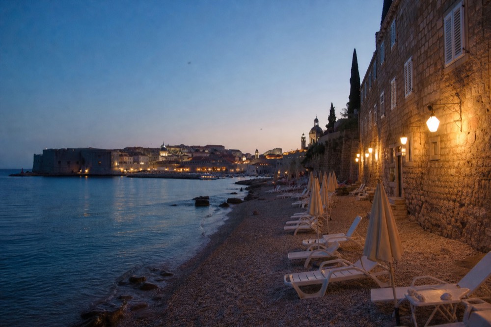 Pebble beach with sun umbrellas and calm clear water near Dubrovnik in summer