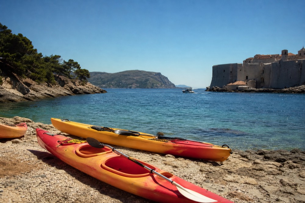 Kayaks resting on a rocky shore beside clear turquoise water near Dubrovnik