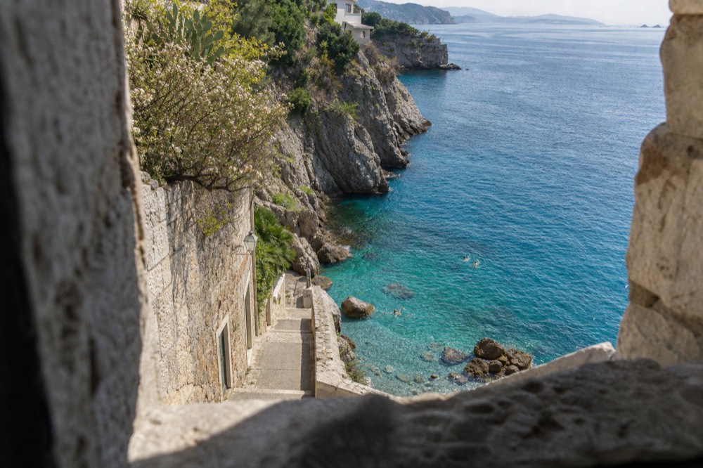 Swimmers in clear turquoise water below rocky cliffs near Dubrovnik