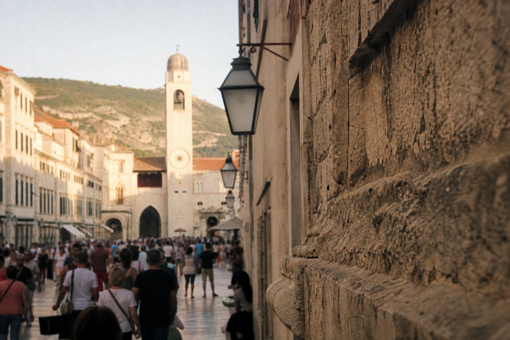A crowded Stradun street with the bell tower at the far end