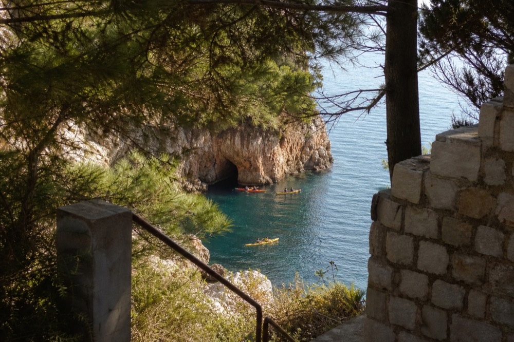 Sea kayaks near a rocky cave entrance on calm morning water