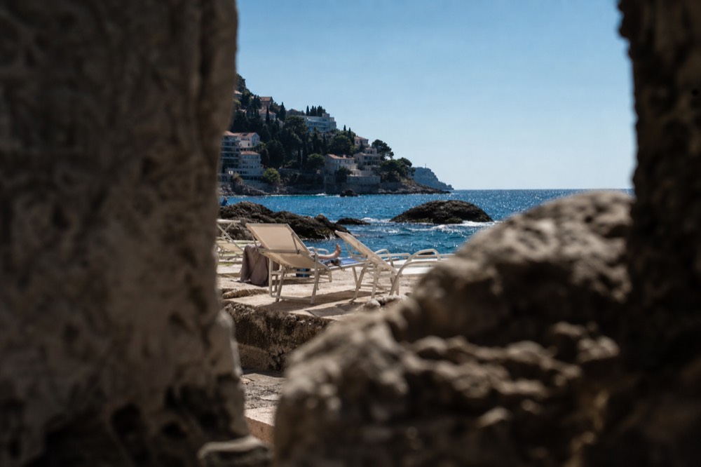 Sunloungers on a stone beach in Dubrovnik under clear autumn sky