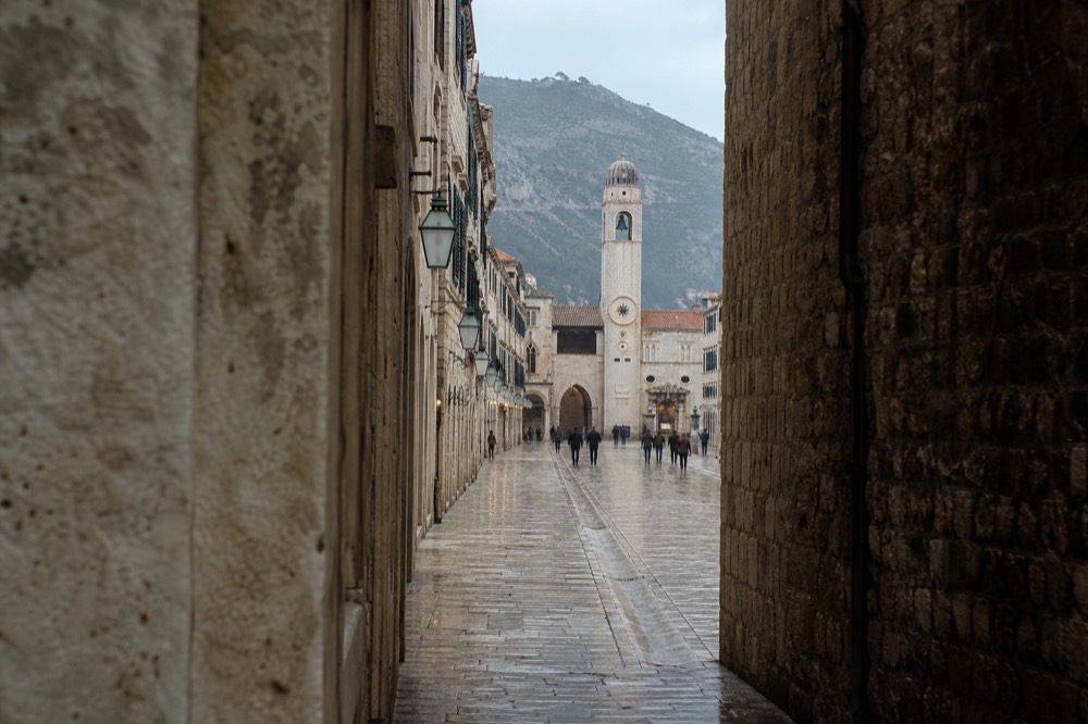 Wet limestone paving of the Stradun reflecting winter light with the bell tower in the distance