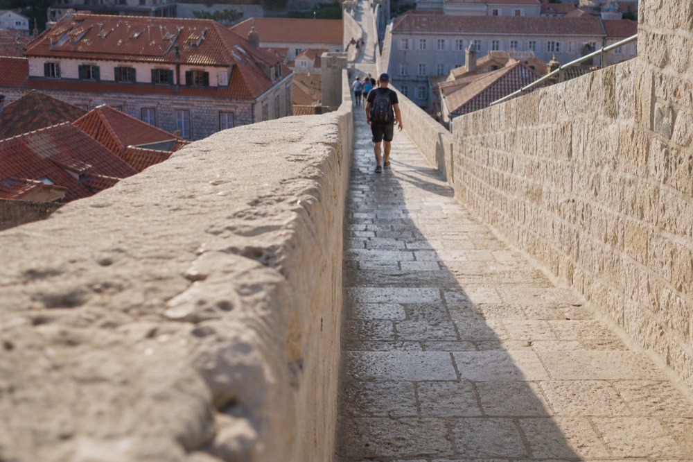 Visitors walking along the top of the city walls with terracotta rooftops of the Old Town below