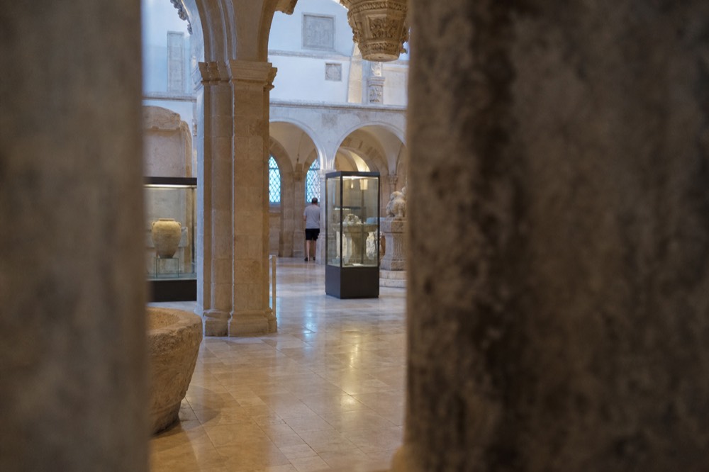 Interior of a museum hall with stone arches, display cases and soft natural lighting