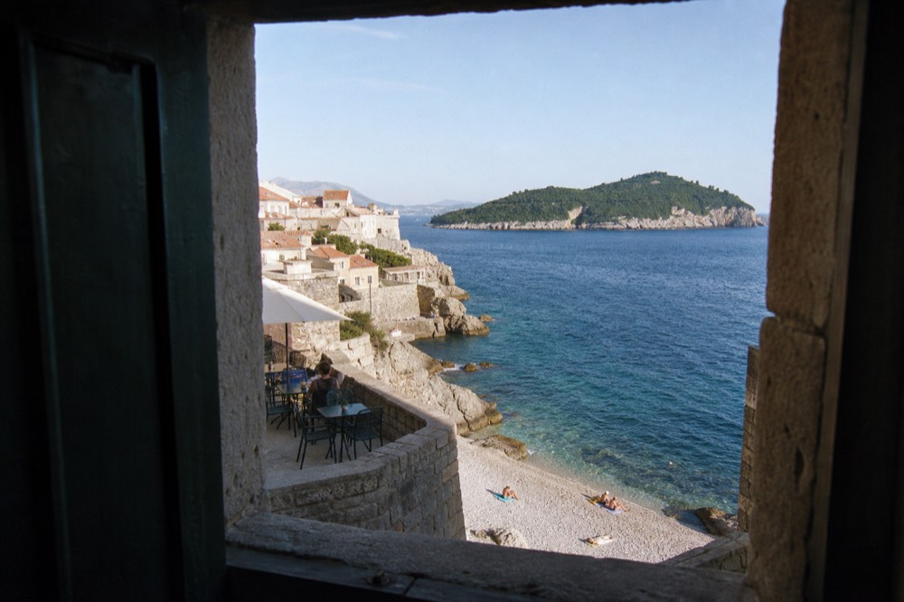A view over red rooftops and a green island toward the Adriatic Sea