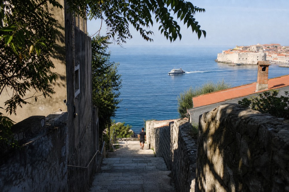 Passenger ferry cutting across open blue water toward a walled coastal town