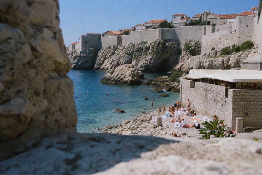 Walled old town seen from the water with terracotta roofs and a fortress on a rock