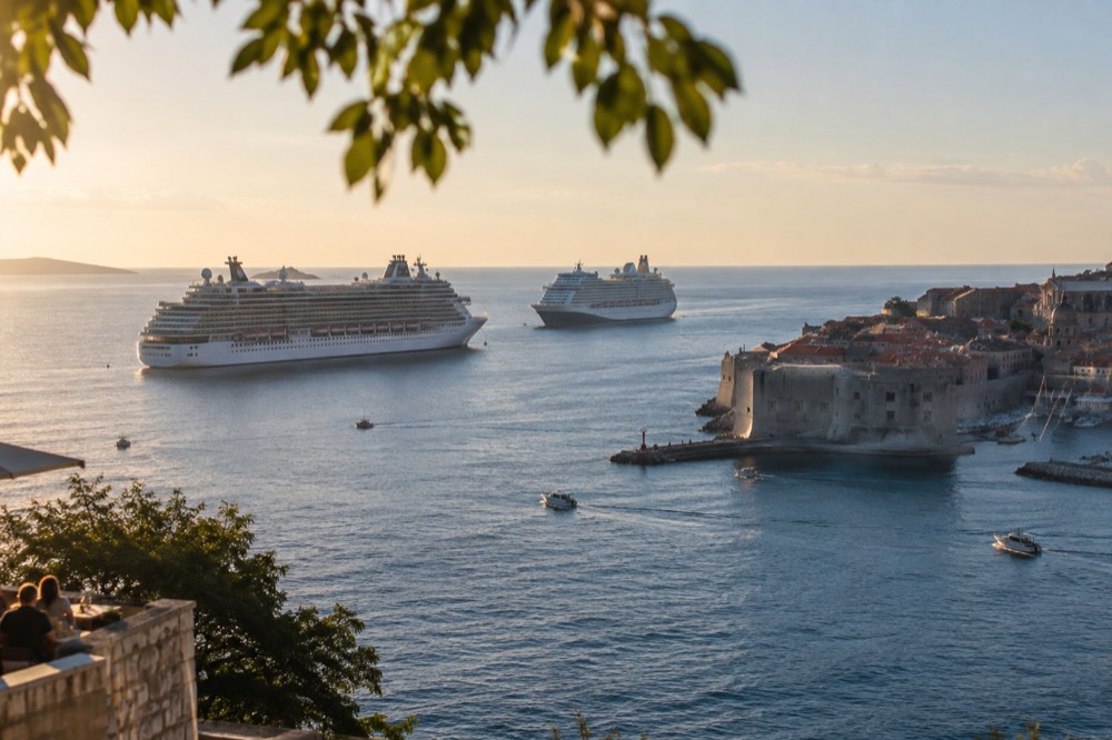 Two cruise ships anchored outside a walled coastal town in morning light