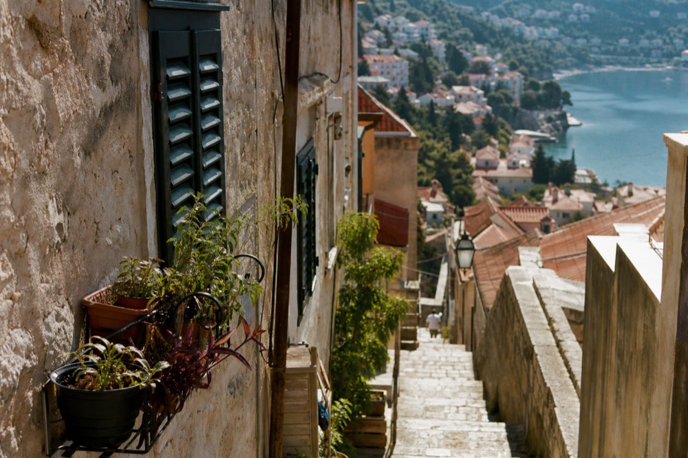 A red-roofed seaside town curving around a calm bay with wooded hills behind