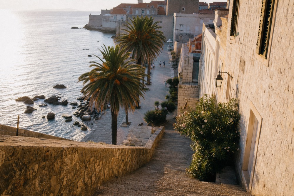 Palm-lined seaside promenade with white stone buildings