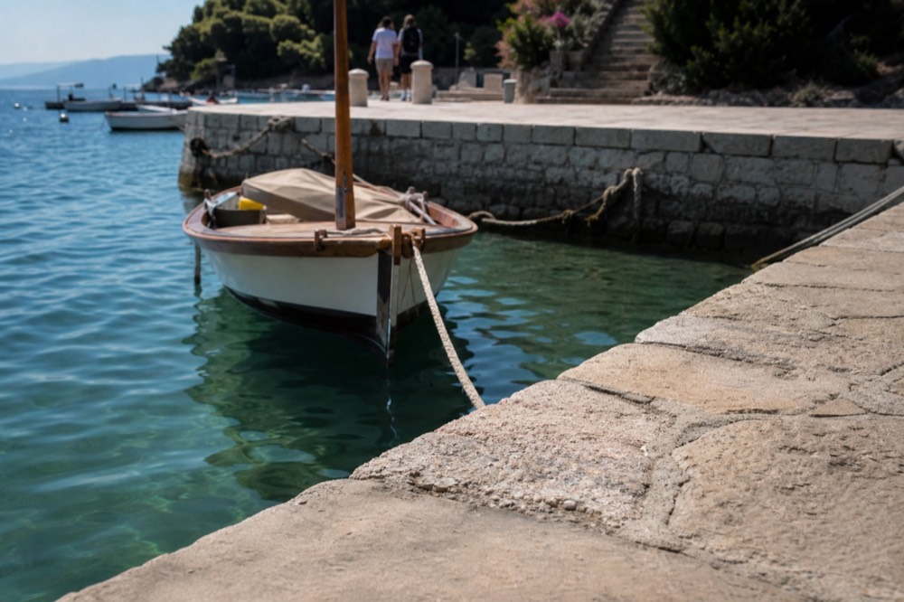 An island boat anchored in clear green water near a stone quay
