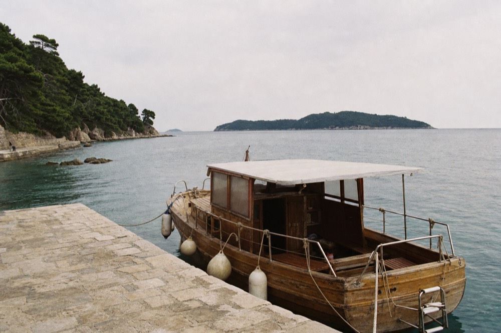 Wooden tourist boat anchored at a stone quay beside clear island water