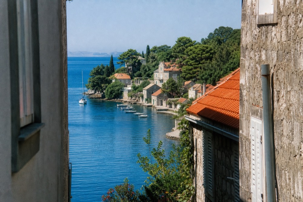Small stone village houses and pine trees along a quiet island shoreline