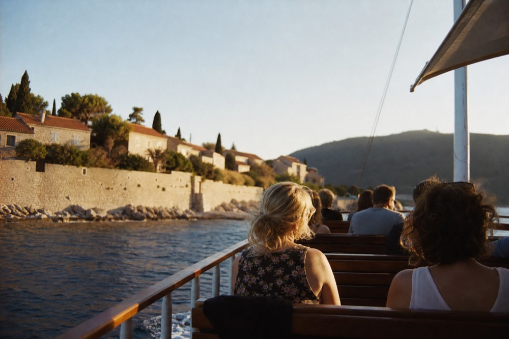 Passengers seated on the deck of a wooden cruise boat leaving a harbour