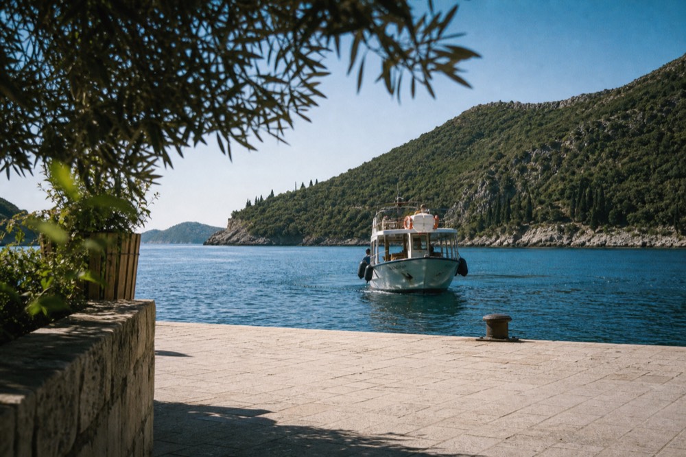 Small ferry boat approaching a stone harbour quay with green island cliffs behind