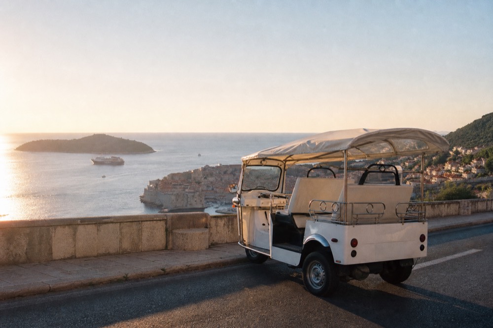 An open-sided tuk-tuk vehicle parked on a coastal road above Dubrovnik with the walled city below