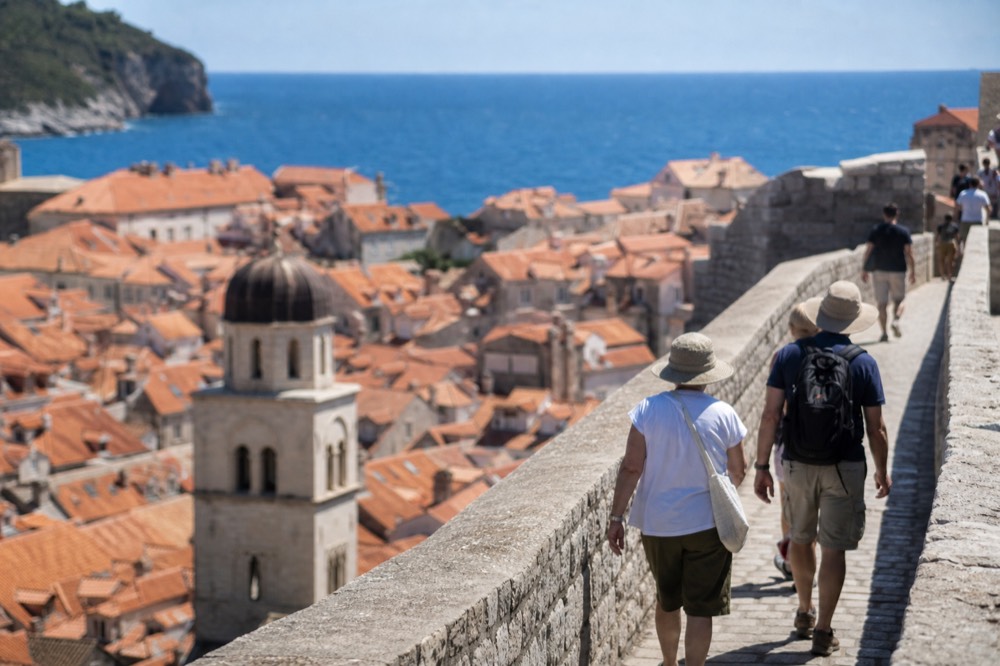 Walkers on the city walls of Dubrovnik with red rooftops and church towers below on a bright day