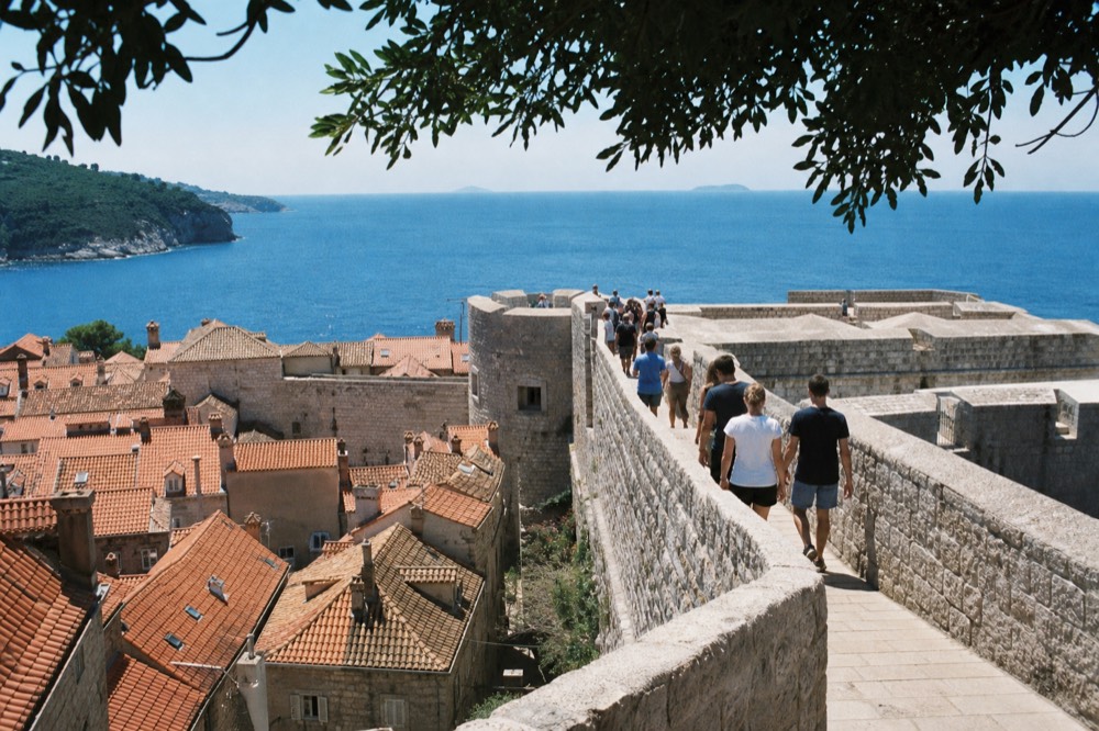 Visitors on the Dubrovnik city walls path above red rooftops with the sea beyond