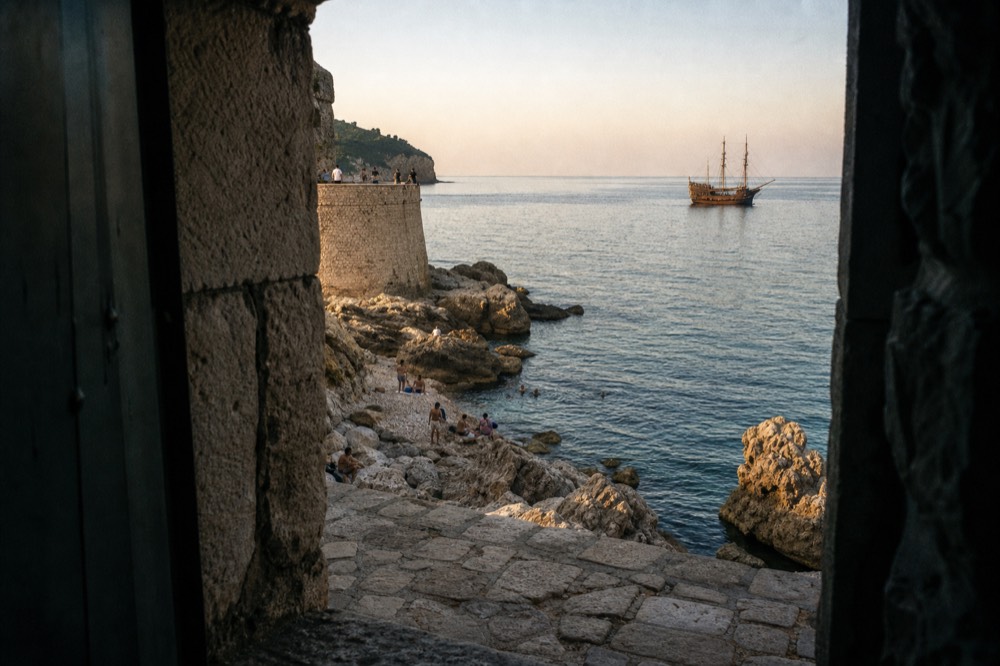 A wooden sailing ship on calm evening water outside Dubrovnik Old Town at sunset