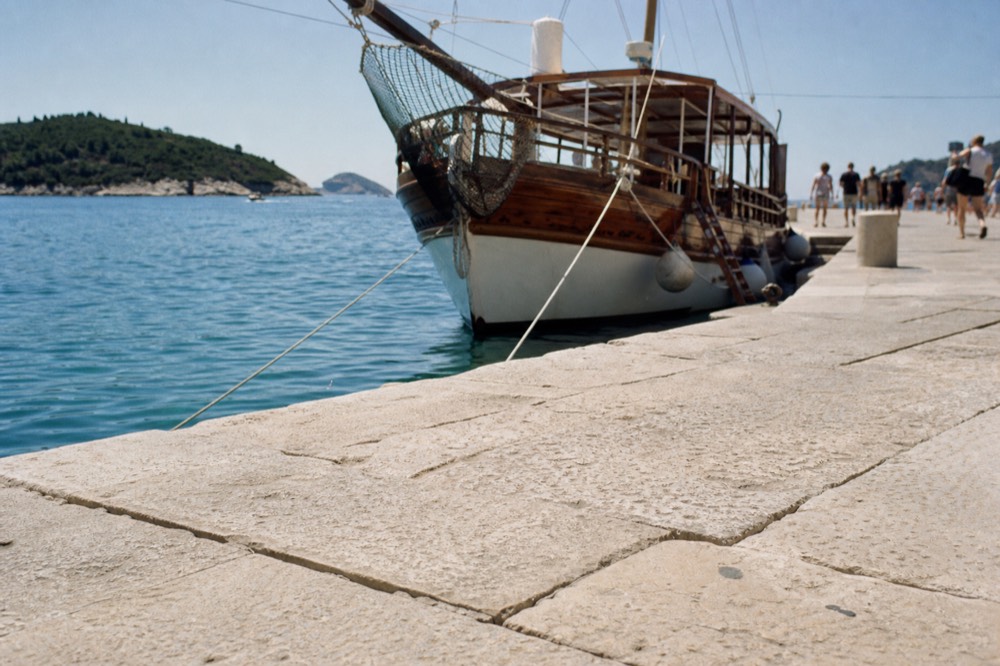 A wooden tour boat anchored beside a stone quay with island hills in the distance