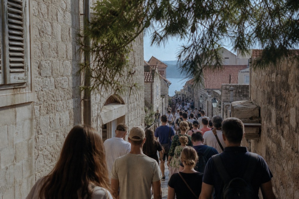 A crowded stone street in Dubrovnik old town with tour groups walking between limestone buildings