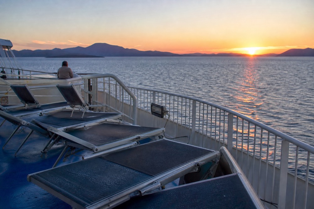An open ferry deck at dusk with the Adriatic horizon and lounge chairs