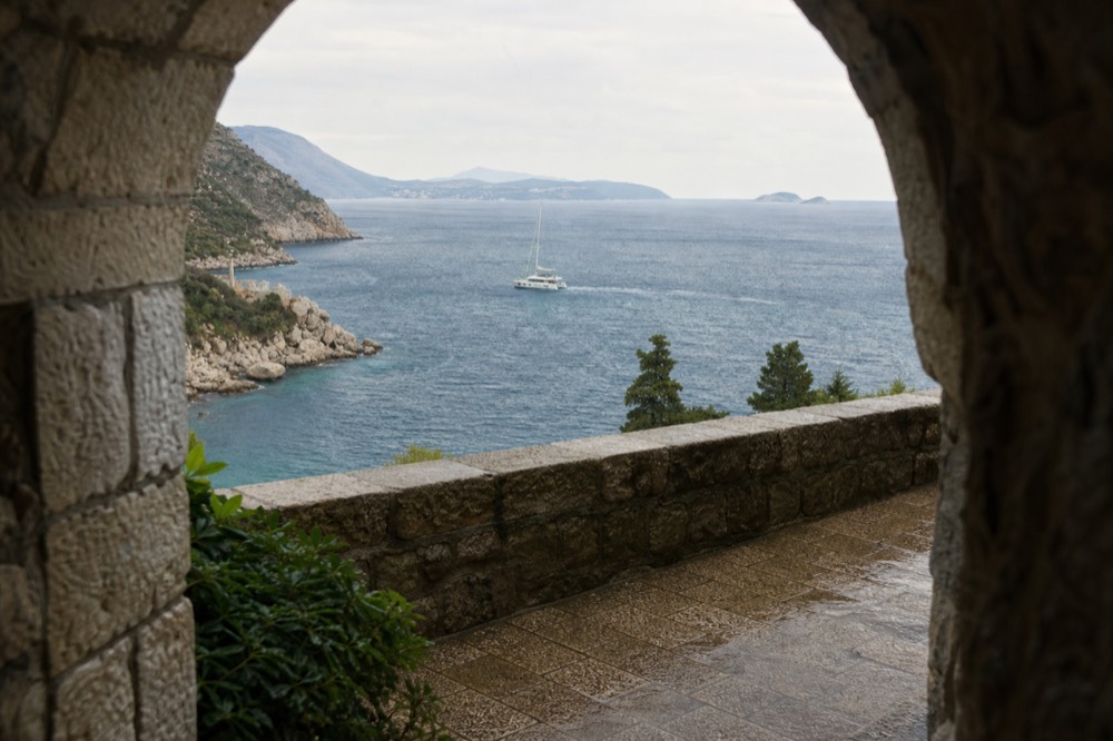 A catamaran cutting across open blue water near a rugged coastline