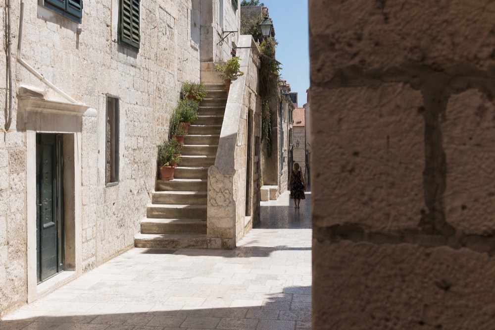 Sunlit limestone street inside Dubrovnik Old Town with shutters and stone staircases
